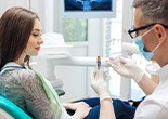 Dentist wearing white showing sample implant to woman with long brown hair.