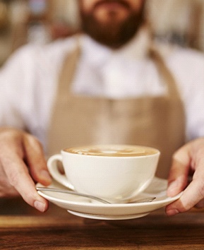 A person holding a cup of coffee that is on a small dish with a spoon