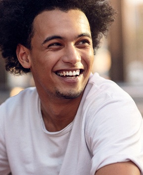 A young man wearing a white t-shirt smiles after finishing his treatment with at-home teeth whitening