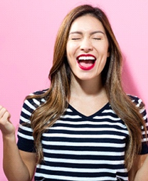 A young woman wearing a striped shirt closes her eyes and expresses excitement in her new smile