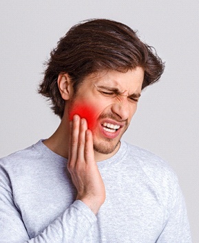 A young male with a beard holding his jaw and cringing in pain while waiting to visit his emergency dentist in Phoenix