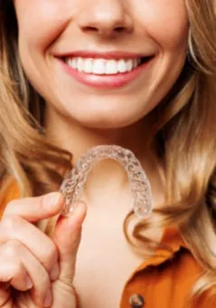 Smiling woman holding an Invisalign clear aligner